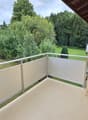 Balcony with white privacy screens, metal railing, and a view of a green garden and trees.