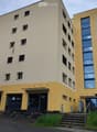 Modern multi-story building with yellow and beige facade, large windows, and a balcony on the upper floor.