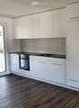 Modern kitchen with white cabinets, black countertops, integrated oven, and sink.