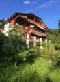 A two-story wooden house with red shutters, balconies, and a well-maintained garden.
