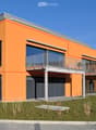 Modern two-story building with orange facade, large windows, balconies, and a garage entrance.