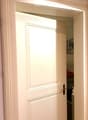 Open doorway leading to another room, with visible interior elements like a bed and artwork in the background.