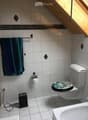 Bathroom with white tiled walls and floor, a toilet, a bathtub, and a towel hanging on the wall.