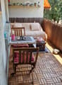 Balcony with wooden decking, sofa, small table, chairs, and potted plants.