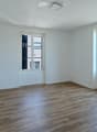 Empty room with white walls, wooden flooring, and large windows offering a view of a green field.