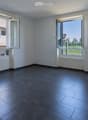 Empty room with dark tiled floor, white walls, and large windows with open shutters, showing a view of the outside area.