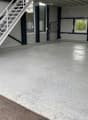 Empty garage with concrete floor, white metal staircase leading up, large windows, and industrial-style doors.