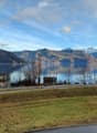 Scenic lakeside view with calm water, distant mountains, and a few houses along the shore.