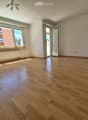 Empty room with wooden flooring, large windows, and a radiator. No furniture or equipment present.