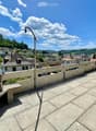 Roof terrace with concrete tiles, low stone walls, and a view of a town and surrounding hills.