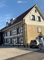 Two-story house with a combination of stone and timber framing, multiple windows with shutters, and a parked car in front.