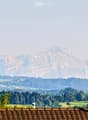 View from a rooftop terrace showing a panoramic landscape with rolling hills, dense forests, and distant mountains under a hazy sky.