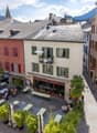 Courtyard with outdoor seating, tables, chairs, potted plants, and a small balcony with greenery and an umbrella.