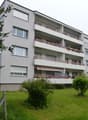 Modern multi-story apartment building with balconies, large windows, and a well-maintained lawn in front.