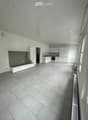 Modern, minimalist kitchen and living area with white cabinets, a built-in bench, and grey tiled flooring.