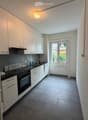 Modern kitchen with white cabinets, black countertops, and stainless steel appliances, including an oven and range hood. The space features a large window with a view of greenery outside.