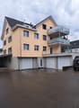Two-story house with beige exterior, multiple windows, garage, and balcony on the upper level.