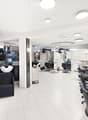 Modern salon with white tiled floors, multiple black and white chairs, mirrors, shelves with hair products, and a reception area with a glass table.