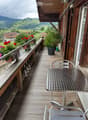 Wooden balcony with metal table and chair, potted plants, and scenic countryside view.