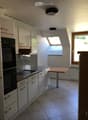 Modern kitchen with white cabinets, granite countertops, induction stove, built-in oven, and a small wooden table.