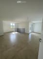 Empty room with tiled floor, white walls, and large windows, featuring a metal safety barrier near the window.