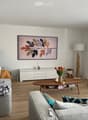 Living room with sofa, coffee table, TV, center table, speaker, white walls, flooring, plants, lamp, cabinet, artwork, remote control