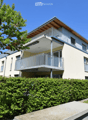 Modern two-story residential building with balconies, surrounded by greenery and a well-maintained lawn.