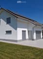 Modern two-story house with white exterior, grey shutters, and a covered driveway. The house features a garage and is surrounded by a well-maintained lawn.