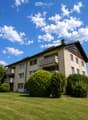 A multi-story residential building with balconies, surrounded by well-maintained green lawns and trees.
