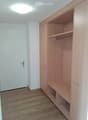 Empty room with wooden floor, white walls, and built-in wooden closet with shelves and hanging rod.