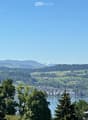 Panoramic view of a lake surrounded by lush green hills and distant mountains under a clear blue sky.