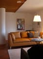 Cozy living room with leather sofa, coffee table, artwork on the walls, and a fireplace. The room has a warm, inviting atmosphere with natural light coming in through the windows.