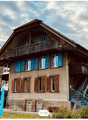 Two-story house with wooden balconies, blue shutters, and a staircase leading to the entrance.