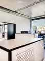Modern office space with white walls, large windows, desks, chairs, and a large screen. A large container is placed on a table near the window.