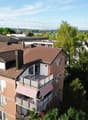 Aerial view of a multi-story residential building with balconies, surrounded by trees and a scenic view of a lake and cityscape in the background.