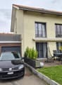 Two-story house with beige exterior, garage, raised ground floor, and outdoor seating area with a dining table and chairs.