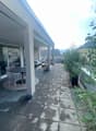 Modern balcony with tiled floor, outdoor furniture including a table and chairs, large glass sliding doors leading to indoor space, and lush green plants.