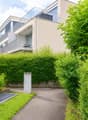 Modern residential building with raised ground floor, surrounded by lush greenery and a well-maintained garden path.