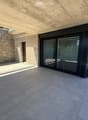 Modern balcony with concrete ceiling, tiled floor, stone wall, and large sliding glass door.