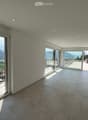 Modern, open-plan room with large glass doors leading to a balcony, tiled floor, bar counter with two stools, and scenic mountain view.