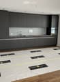 Modern kitchen with dark grey cabinets, a sink, and a wooden floor. Protective plastic sheets are laid out on the floor, likely for renovation or installation purposes.