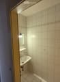 Small bathroom with white tiled walls and floor, a white sink, a mirror, and a light fixture above the sink.