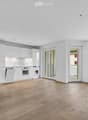 Completely empty room with wooden flooring, white walls, and modern white kitchen cabinets visible in the background. No furniture or equipment present.