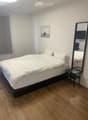A modern bedroom with a neatly made bed, a large mirror, a nightstand, and a picture frame on the wall.