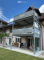 Modern two-story house with a large balcony and patio area, featuring outdoor furniture and a well-maintained lawn.