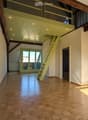 Bright, open loft space with exposed wooden beams, polished wooden floor, large windows, and a small staircase leading to an upper level.