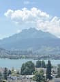 Panoramic view of a cityscape with a lake, mountains, and scattered buildings.