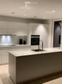 Modern kitchen with white cabinetry, a central island, and marble countertops. Features include a sink with a modern faucet, an oven, and decorative elements like a plant and a vase with dried flowers.