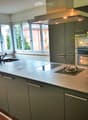 Modern kitchen with grey cabinets, a central island with a sink and stove, and large windows overlooking the street.