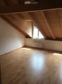 Empty attic room with wooden floor, exposed wooden beams, and a single window letting in natural light.